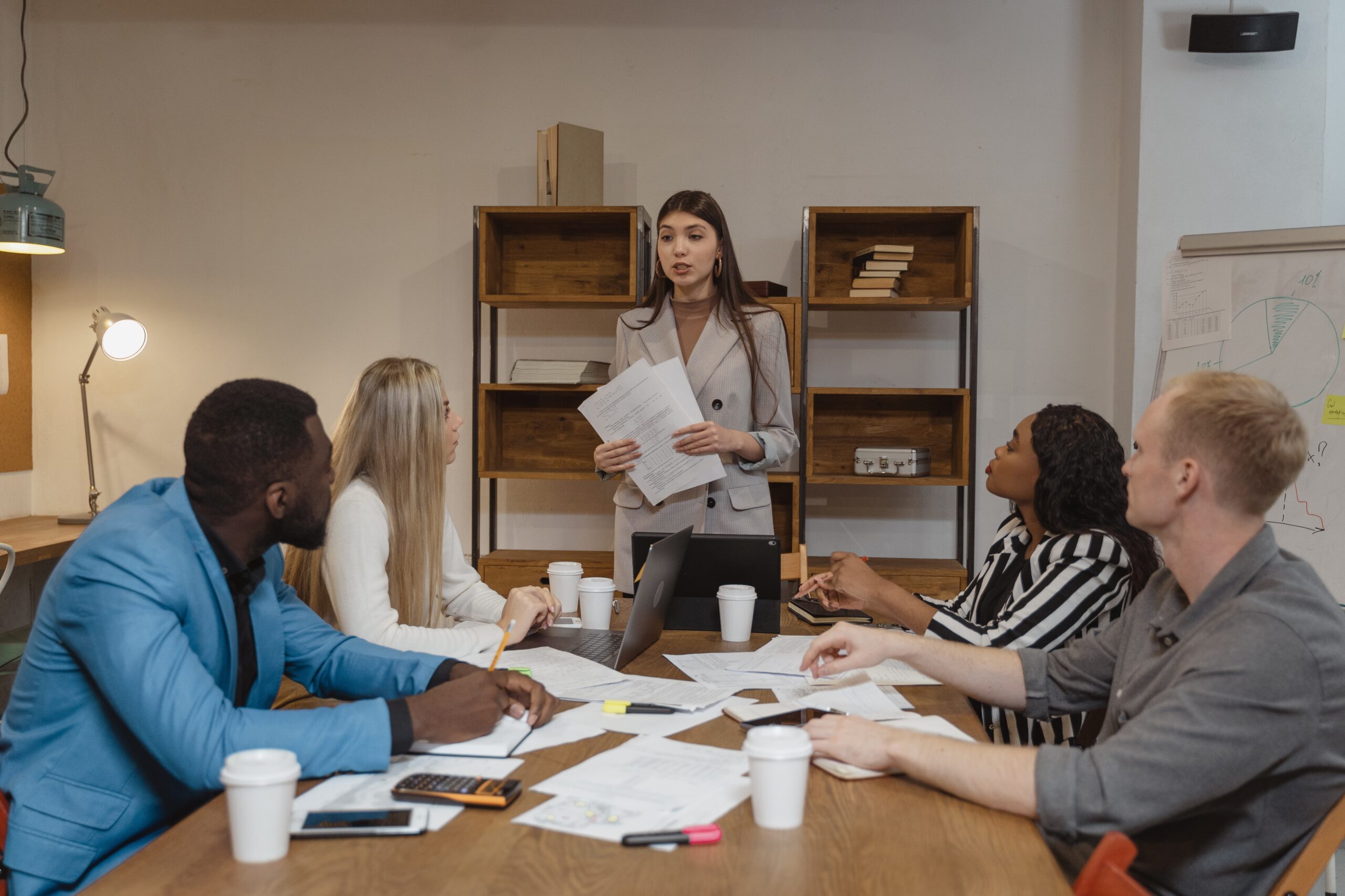 One Person Standing In Front of a Desk With People Listening to Them