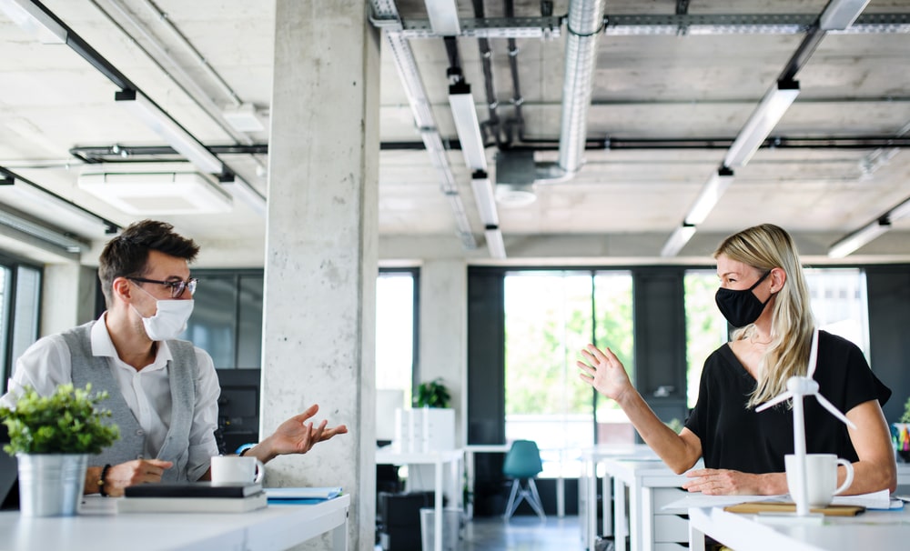 Two People In The Office With Masks On Talking