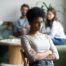 Closeup of a woman with arms crossed avoiding conflict with employees in the background