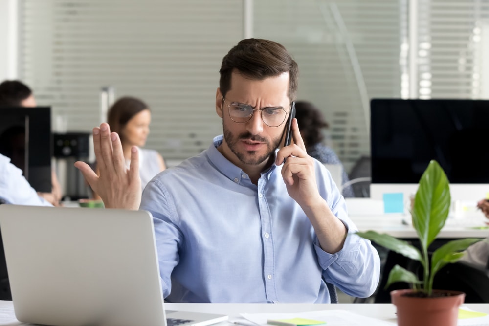 Angry business man talking on phone disputing looking at laptop, stressed frustrated office worker arguing by mobile solving online computer problem with technical support complaining on bad service